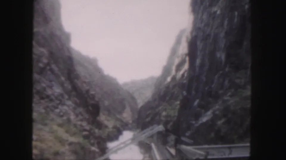 1958 Colorado home-movie frame looking along a narrow canyon, with bridge railing and water visible below.