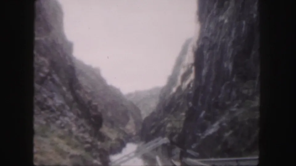 1958 Colorado 8mm frame showing a narrow river through steep rocky walls, with a cable or bridge-like structure spanning the canyon.