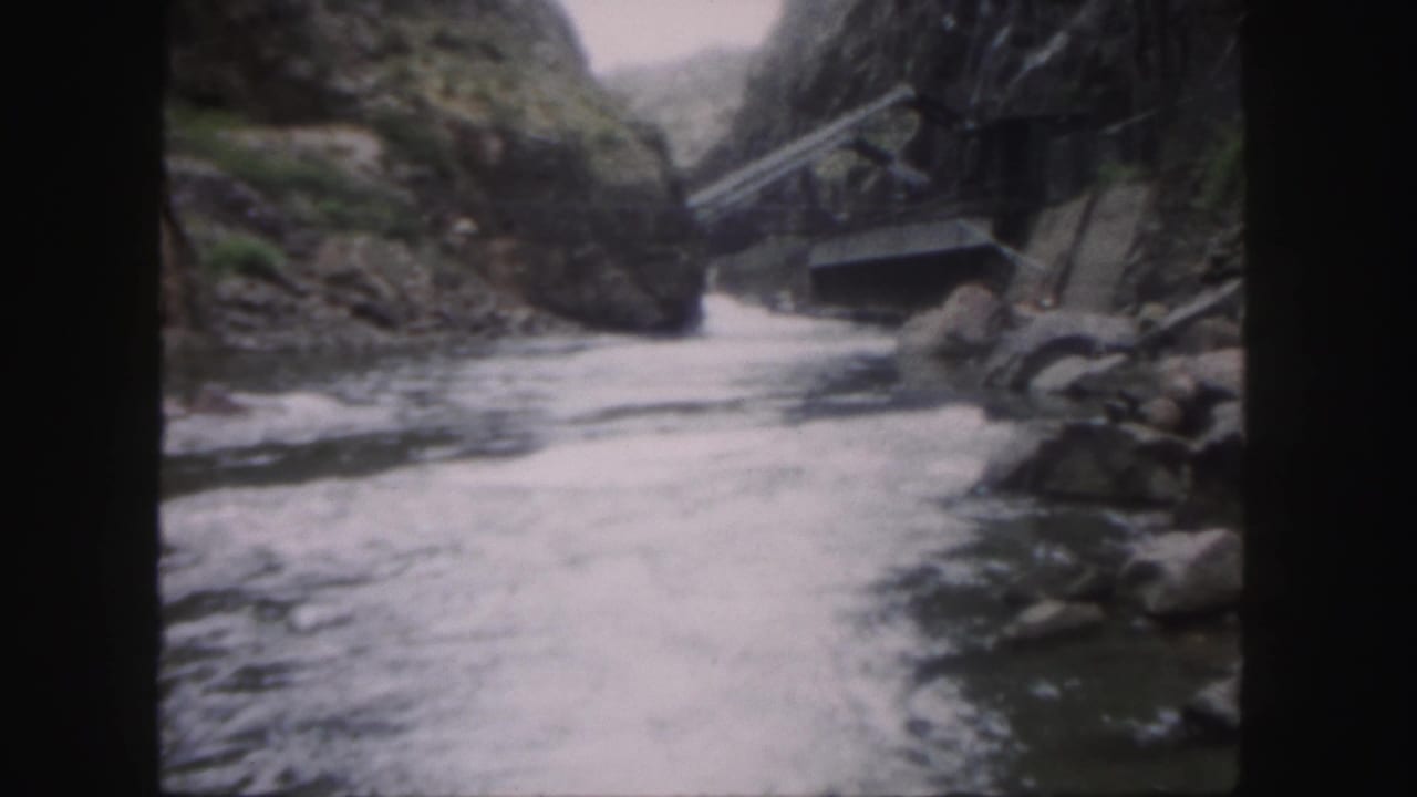 1958 Colorado 8mm frame showing whitewater moving through a rocky canyon toward a small weathered bridge.