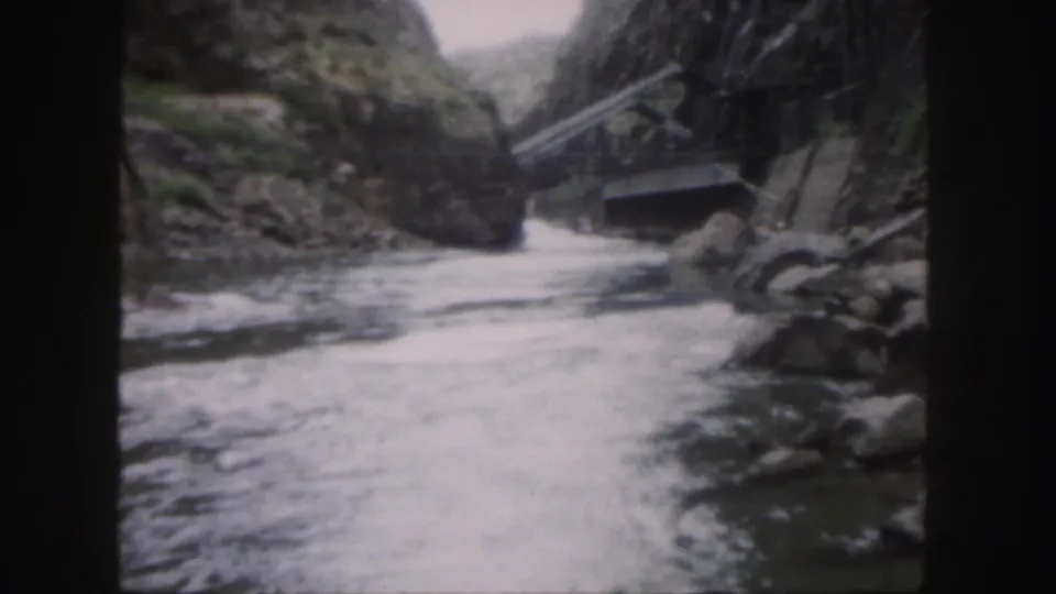 1958 Colorado 8mm frame showing whitewater moving through a rocky canyon toward a small weathered bridge.