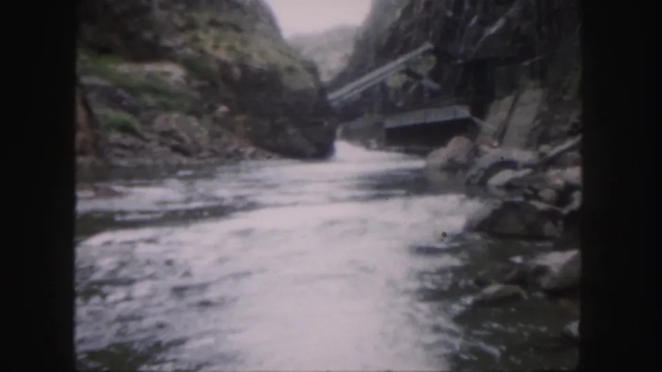 Soft 8mm Colorado canyon view with white rapids, boulders, steep rock faces, and bridge railings above the right side.