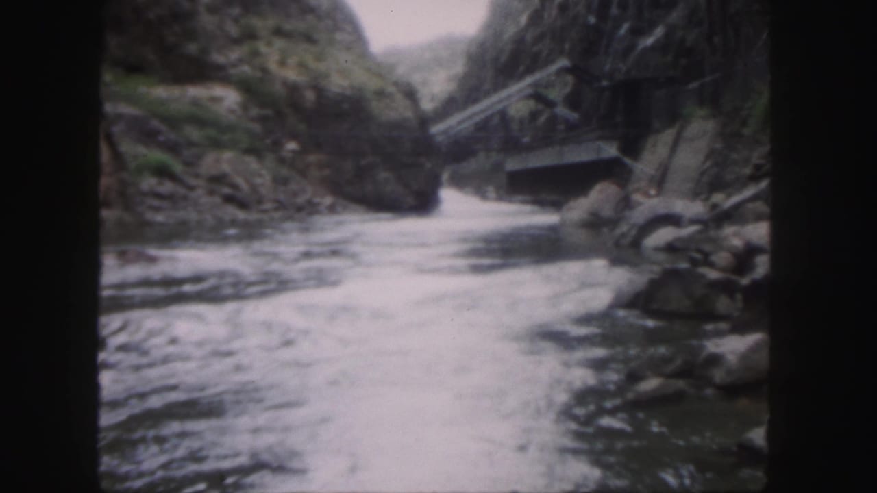 1958 Colorado 8mm frame showing fast river water moving between rocky canyon walls, with a small structure or crossing visible on the right.