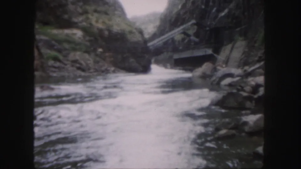 1958 Colorado 8mm frame showing fast river water moving between rocky canyon walls, with a small structure or crossing visible on the right.