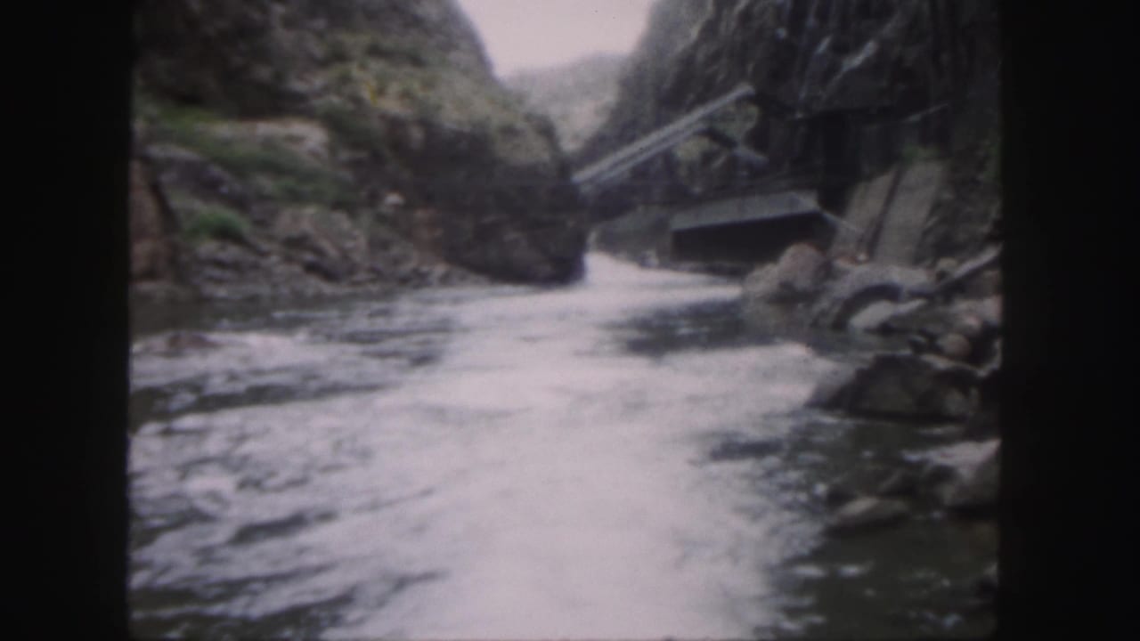 1958 Colorado home-movie frame of turbulent river water passing through a narrow rocky canyon, with a small crossing or built element at right.