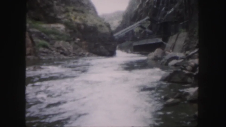 1958 Colorado home-movie frame of turbulent river water passing through a narrow rocky canyon, with a small crossing or built element at right.