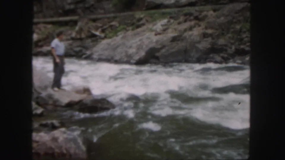In Colorado 1958 home-movie footage, a man stands on a rocky edge beside churning river currents.