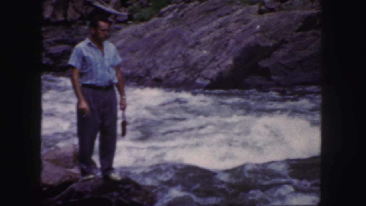 Man standing on rocks beside rushing river water.