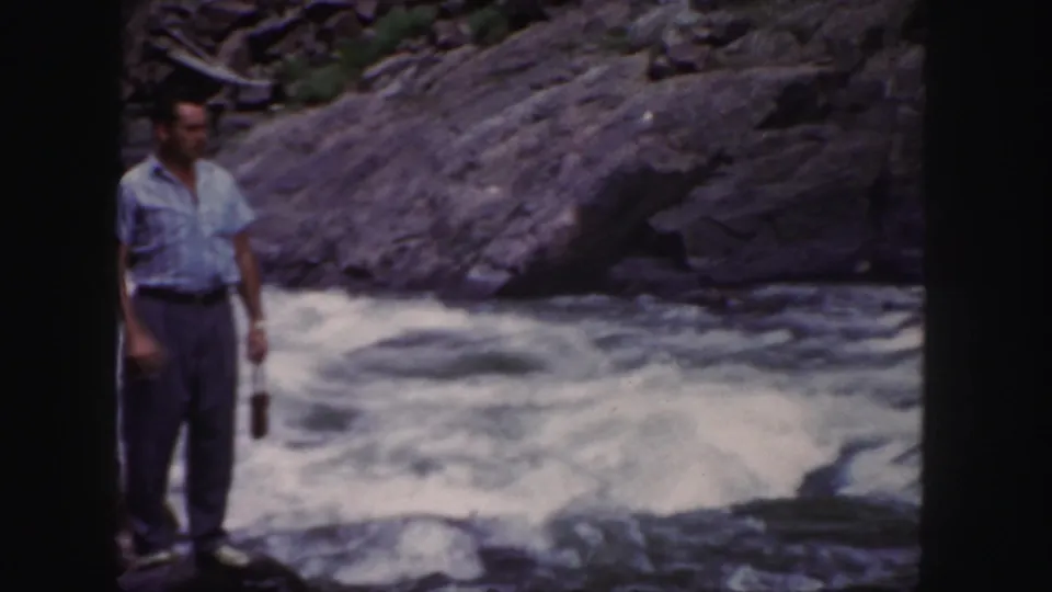 The man remains near the Colorado river, holding a small object while whitewater moves behind him.