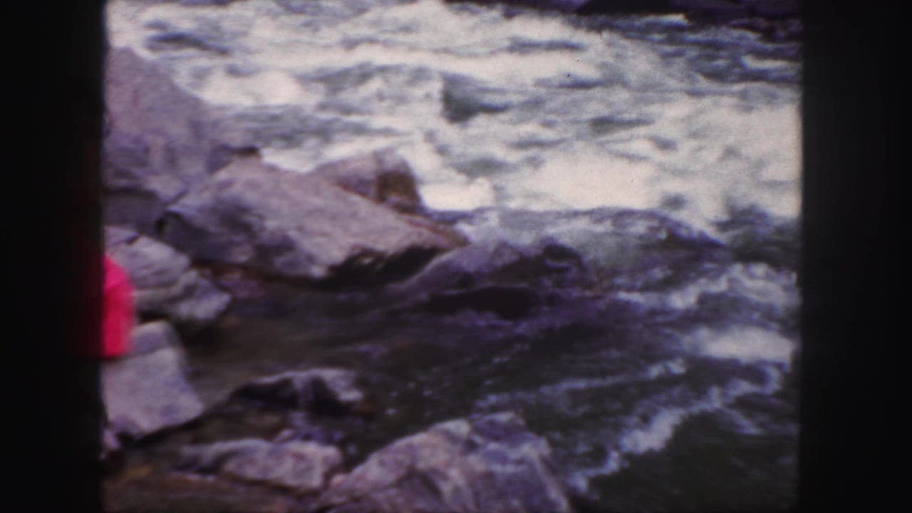 Rocky river scene with part of a red dress visible at the left edge.