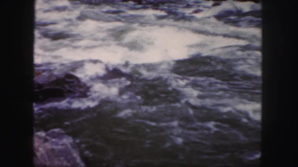 1958 Colorado home-movie frame showing turbulent river water, rocks, and prominent 8mm film gate edges.