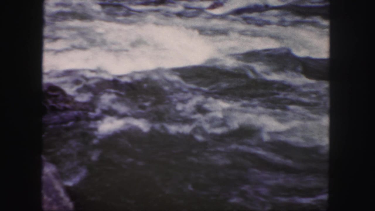 Turbulent river water in a Colorado home-movie frame, with soft 8mm grain and dark frame edges.