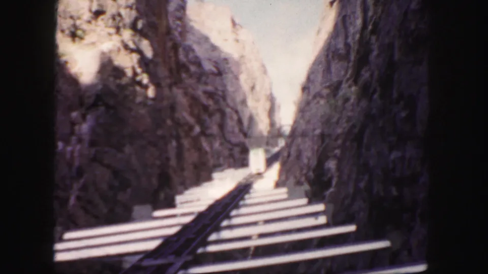 A rocky Colorado gorge or canyon passage appears in 8mm footage, with water and a narrow rail or walkway visible below.