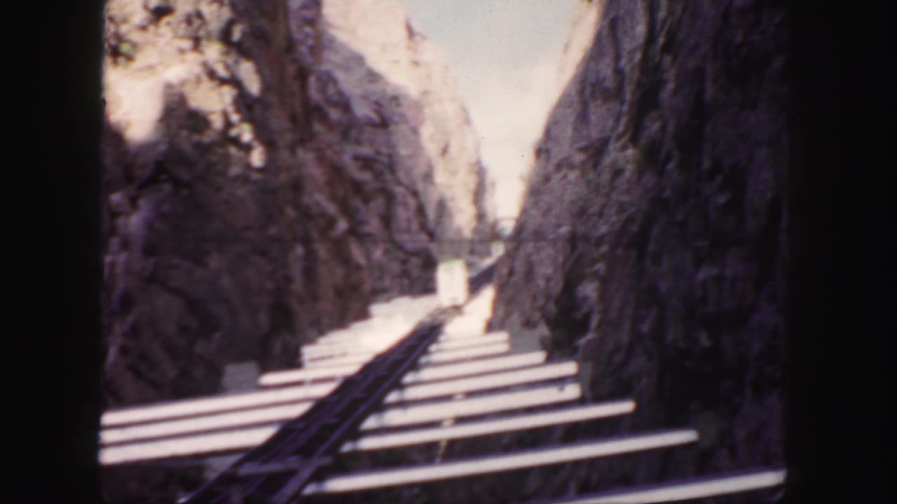 1958 Colorado 8mm frame looking forward along railway rails and pale ties through a narrow rocky canyon.