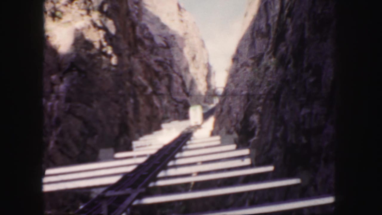 Colorado home-movie view of rails and wooden ties passing through a rocky canyon, with a small rail car ahead.