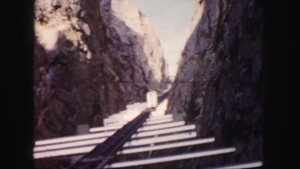 Colorado 8mm frame with rails and ties leading through a rocky canyon toward a small distant rail car.