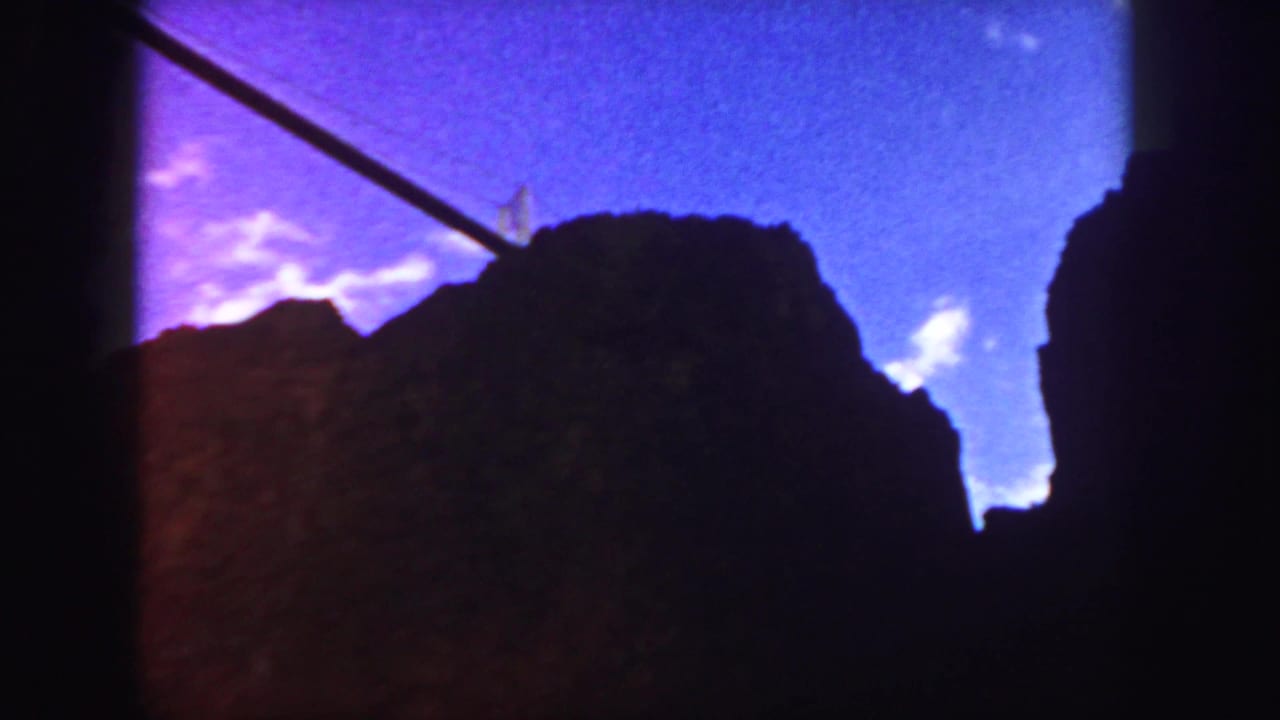 1958 Colorado 8mm frame with dark rock or temple-like silhouettes under a vivid purple-blue sky and a diagonal cable or rail.