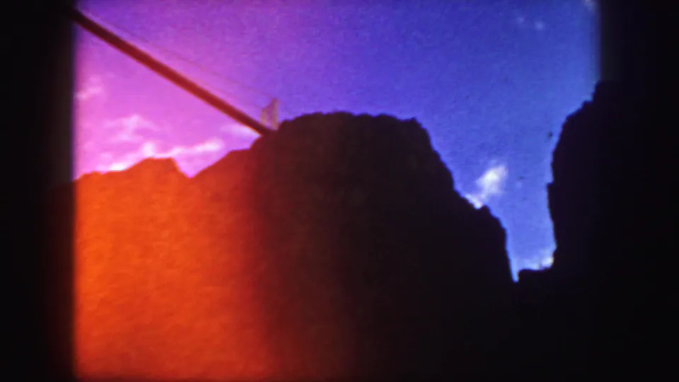 1958 Colorado 8mm frame with a silhouetted rock or temple-like form, orange exposure flare and a purple-blue sky.