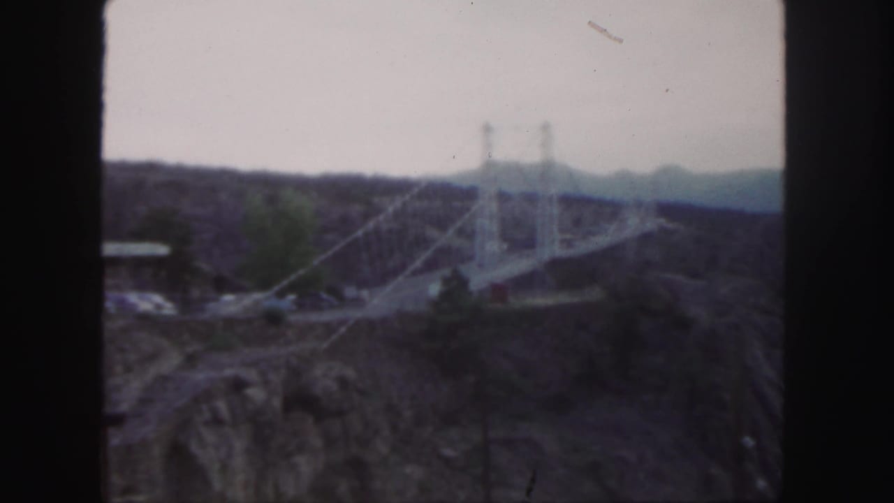 White suspension bridge and canyon seen from a distant overlook.