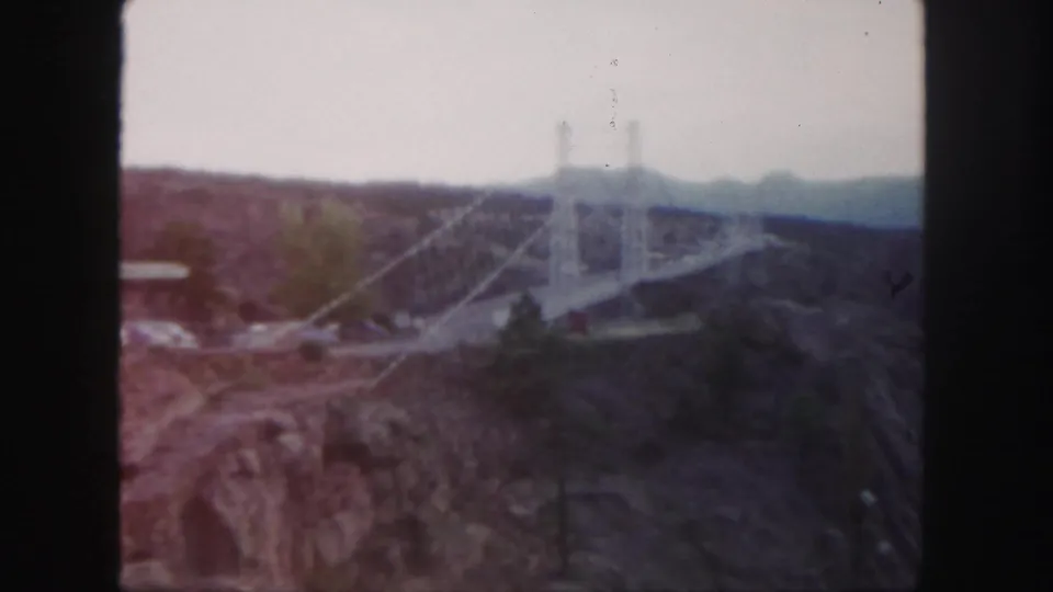 Final 8mm frame holds on the white suspension bridge across a rugged Colorado canyon with muted color and visible film wear.