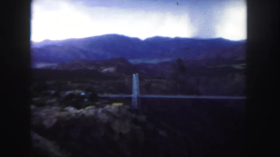 Late frame from the 1958 Colorado home movie, showing a darker mountain and canyon view with part of the suspension bridge visible.