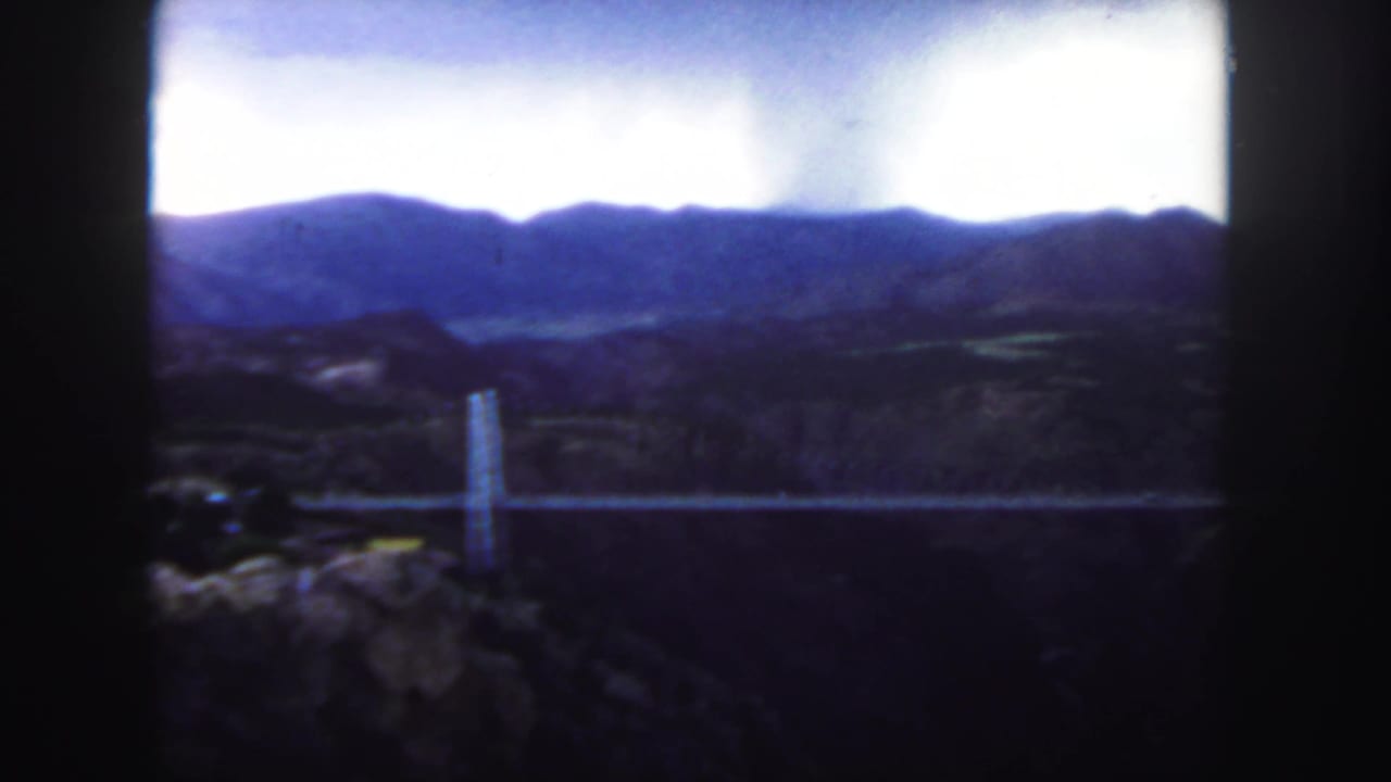 Suspension bridge and canyon landscape appear under a bright overcast sky.