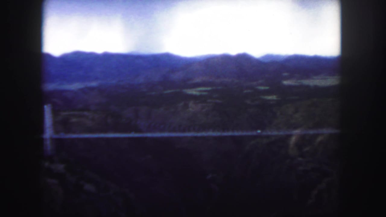 Distant bridge crossing a canyon with dark hills and bright sky.
