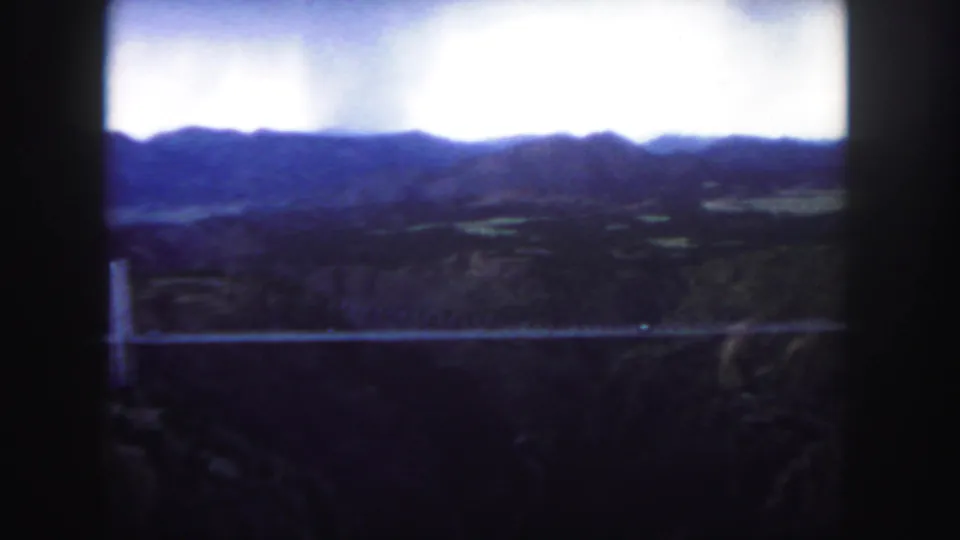 1958 Colorado 8mm frame showing a long bridge spanning a canyon below distant ridges and a bright overcast sky.