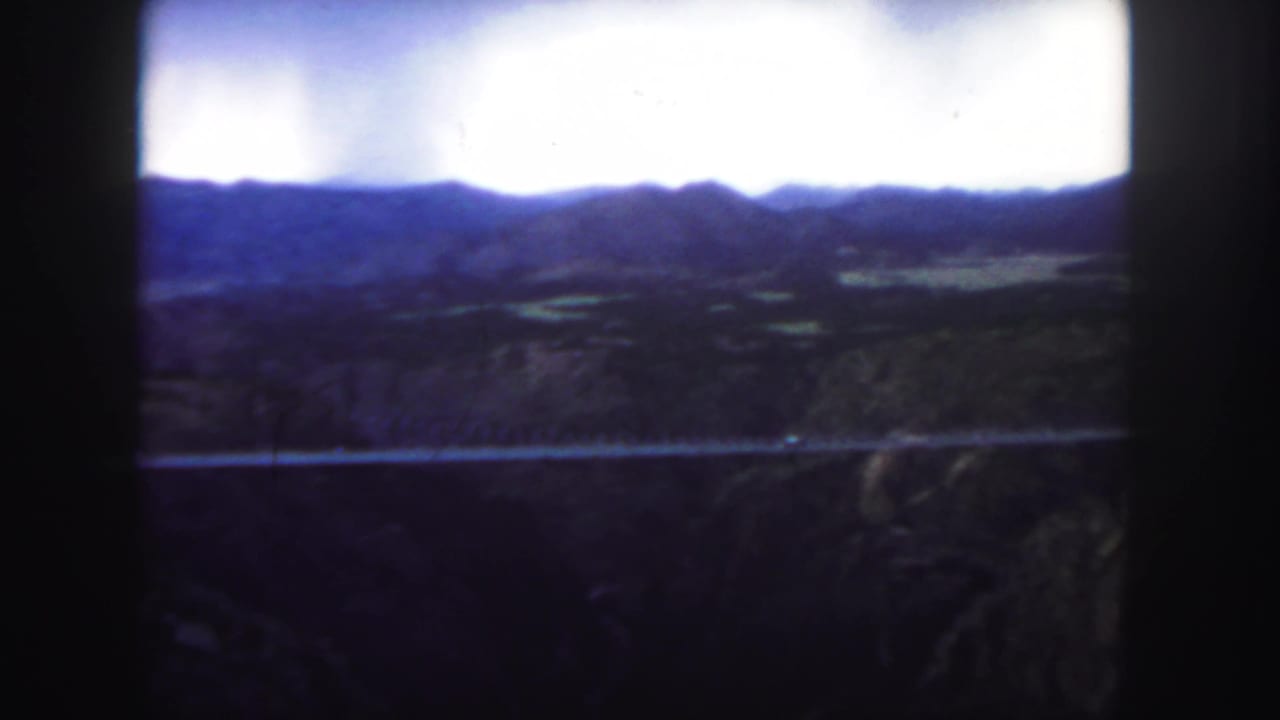 1958 Colorado home-movie view of a bridge crossing rugged canyon terrain with low mountains on the horizon.