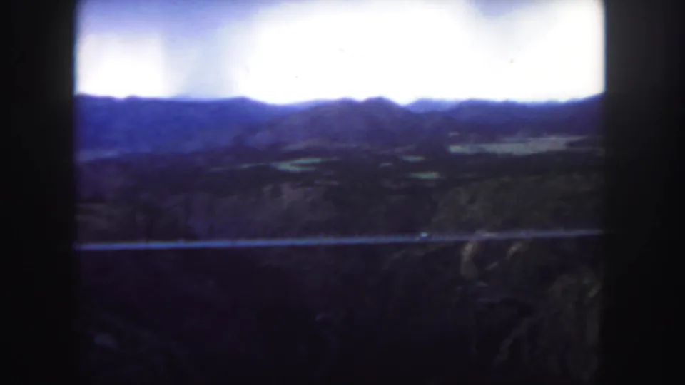 1958 Colorado home-movie view of a bridge crossing rugged canyon terrain with low mountains on the horizon.