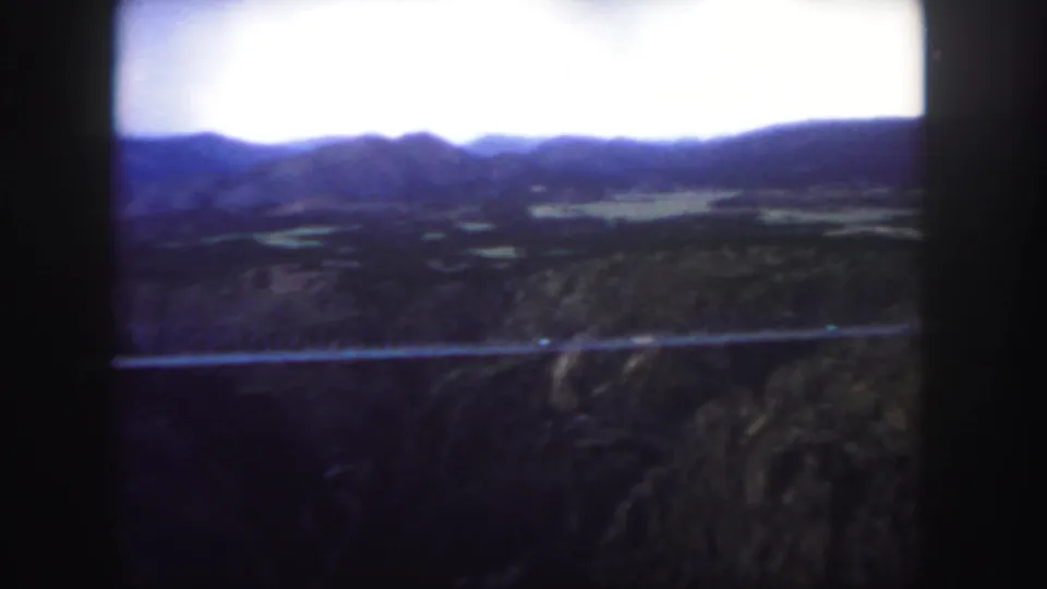 Final 1958 Colorado frame showing the canyon bridge, dark foreground terrain, distant hills, and bright sky in soft 8mm color.