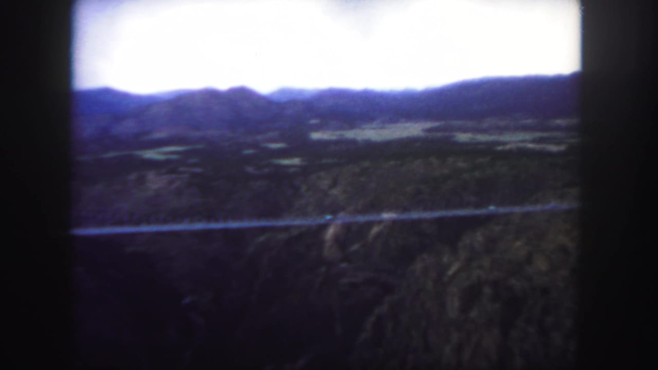 Distant suspension bridge crossing a canyon below dark mountain ridges.