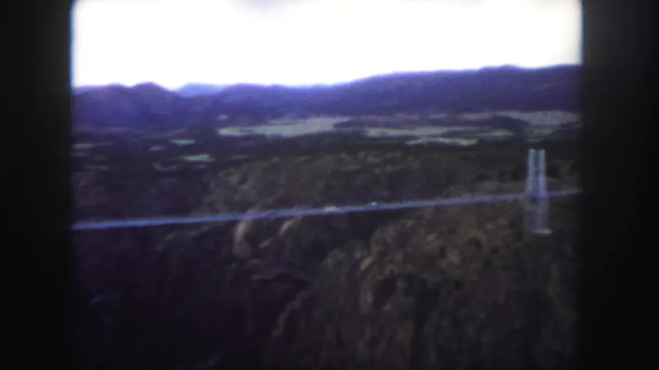 1958 Colorado 8mm still with a bridge span crossing the lower frame and a tower visible against the canyon wall.