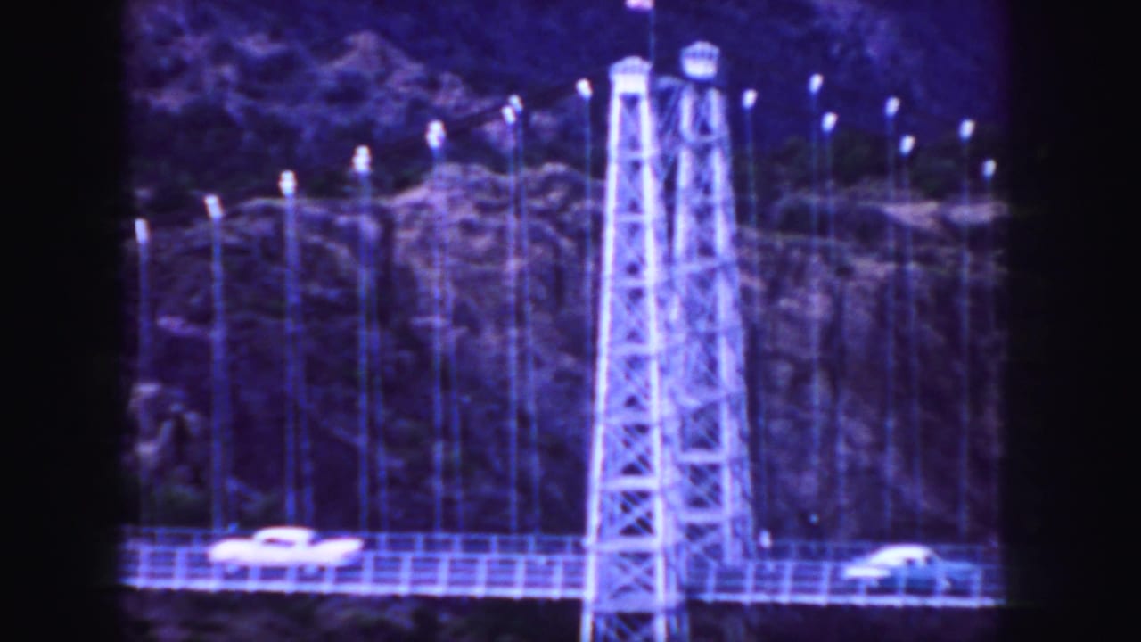 1958 Colorado 8mm frame with classic cars crossing a suspension bridge in front of dark rocky terrain.