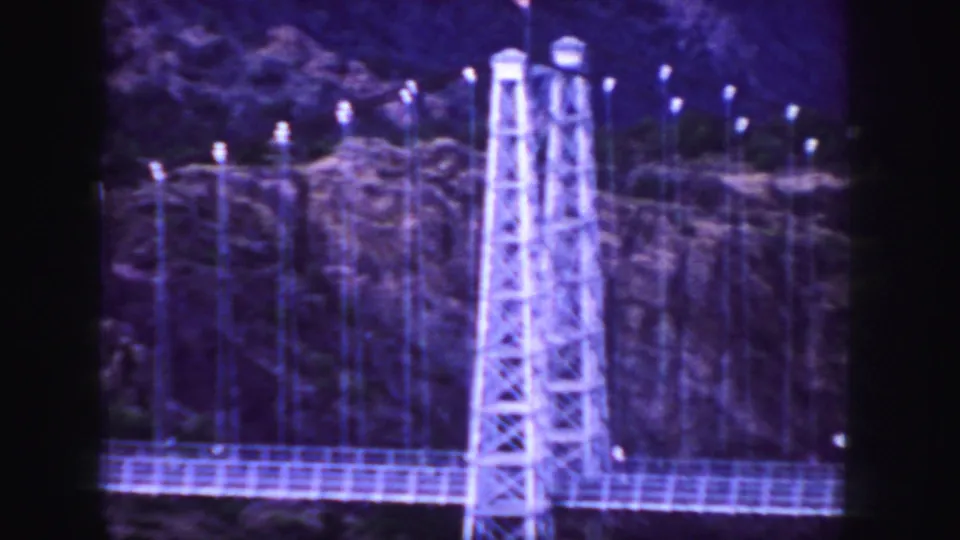 1958 Colorado 8mm frame showing the suspension bridge structure, rocky cliff, and a vehicle near the edge of the span.