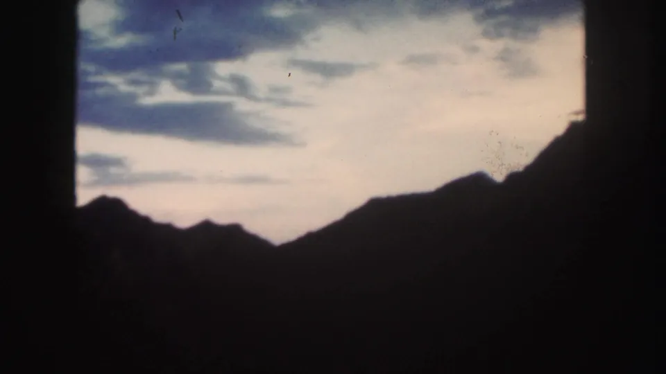 Silhouetted Colorado mountain ridges under a clouded sky, captured with dim exposure and aged 8mm color shift.