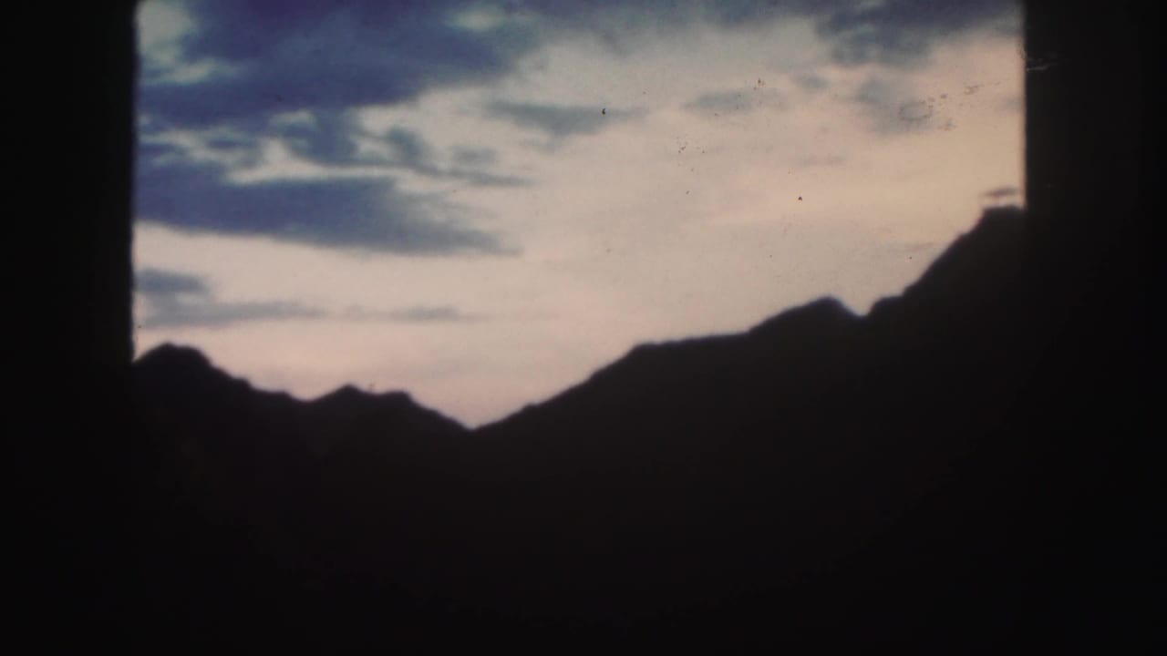 1958 Colorado 8mm frame showing a dark mountain ridge beneath a softly colored cloudy sky, bordered by black film edges.