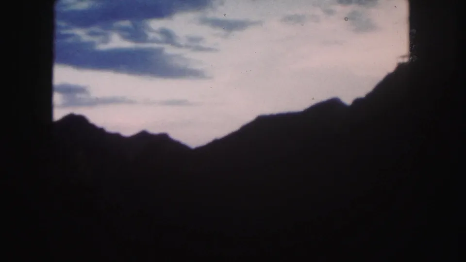 1958 Colorado 8mm still showing a low mountain silhouette against a pastel cloudy sky, with visible grain and dark edge framing.