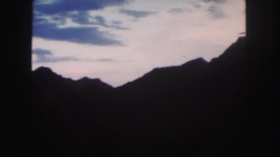 1958 Colorado frame showing silhouetted mountains below a blue-pink cloudy sky, with soft focus and dark film borders.