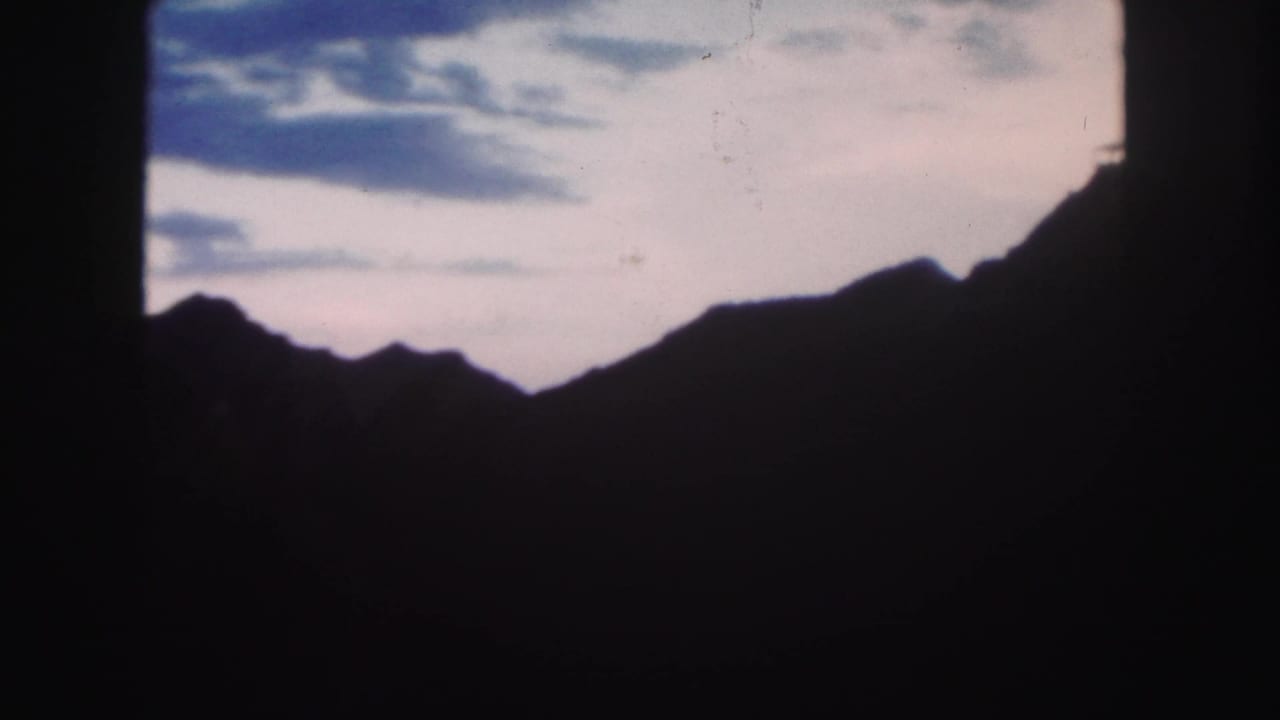 Colorado 1958 home-movie frame showing a dark mountain ridge silhouetted against a fading twilight sky.