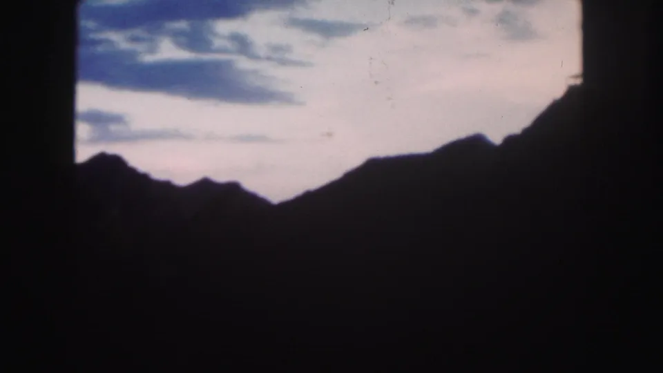 Colorado 1958 home-movie frame showing a dark mountain ridge silhouetted against a fading twilight sky.