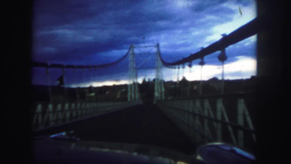 Colorado 1958 home-movie view moving across a suspension bridge beneath a saturated blue twilight sky.
