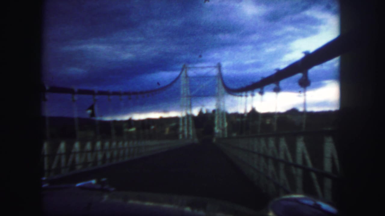 Suspension bridge roadway and cables framed by a vehicle windshield area.