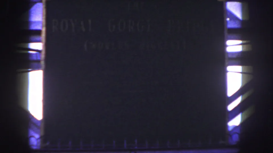 Soft 8mm close-up of the Royal Gorge Bridge plaque in Canon City, Colorado, with dark lettering and bright structural gaps at the sides.