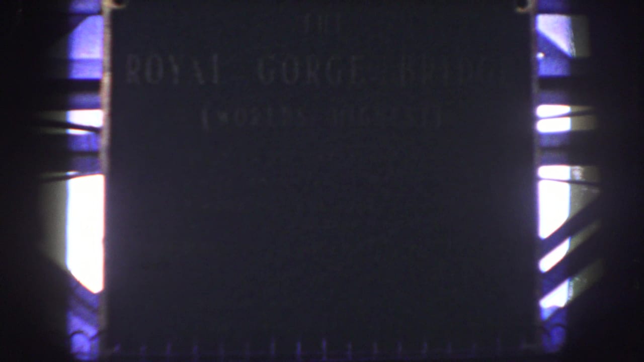 1958 Colorado 8mm frame showing a dark Royal Gorge Bridge plaque with faint lettering and bright light at the frame edges.