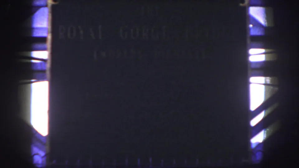 1958 Colorado 8mm frame showing a dark Royal Gorge Bridge plaque with faint lettering and bright light at the frame edges.