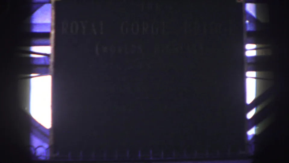 Final 8mm frame of the Royal Gorge Bridge plaque, showing soft lettering, dark stone surface, and bright side illumination.