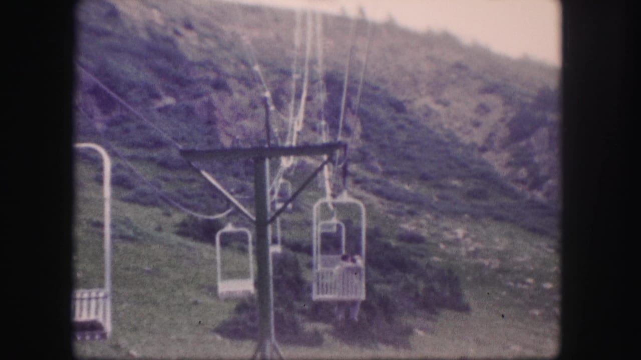 Several chairlift seats move along cables beside a mountain hillside.