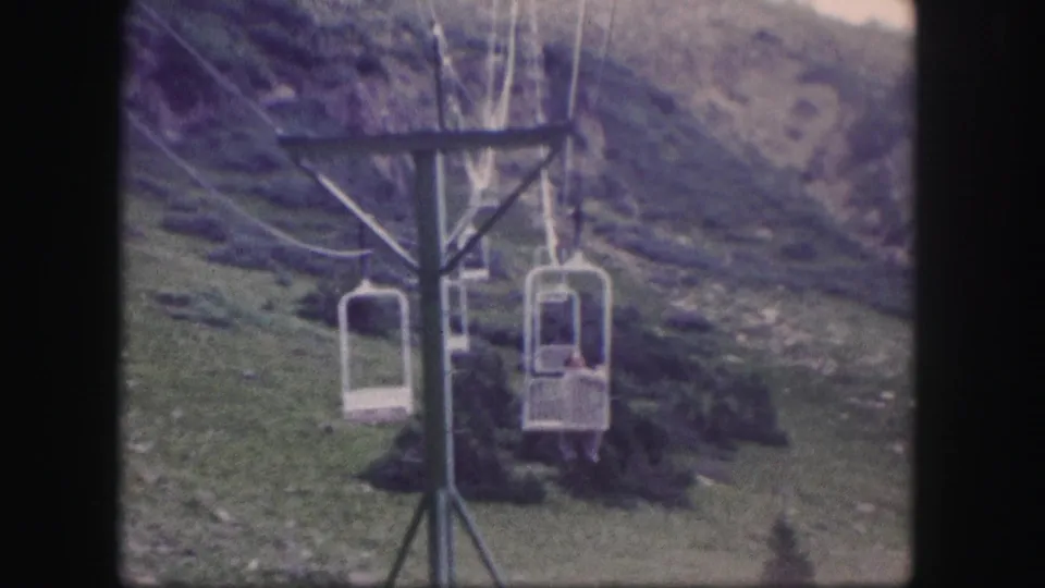 1958 Colorado 8mm frame showing chairlifts near a tower, including one occupied seat on the mountain lift.