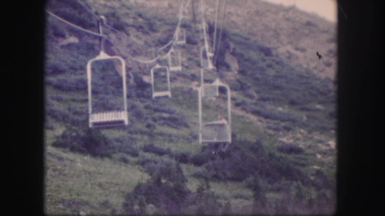 Open chairlift seats rising over a green mountain slope with cables and support towers.