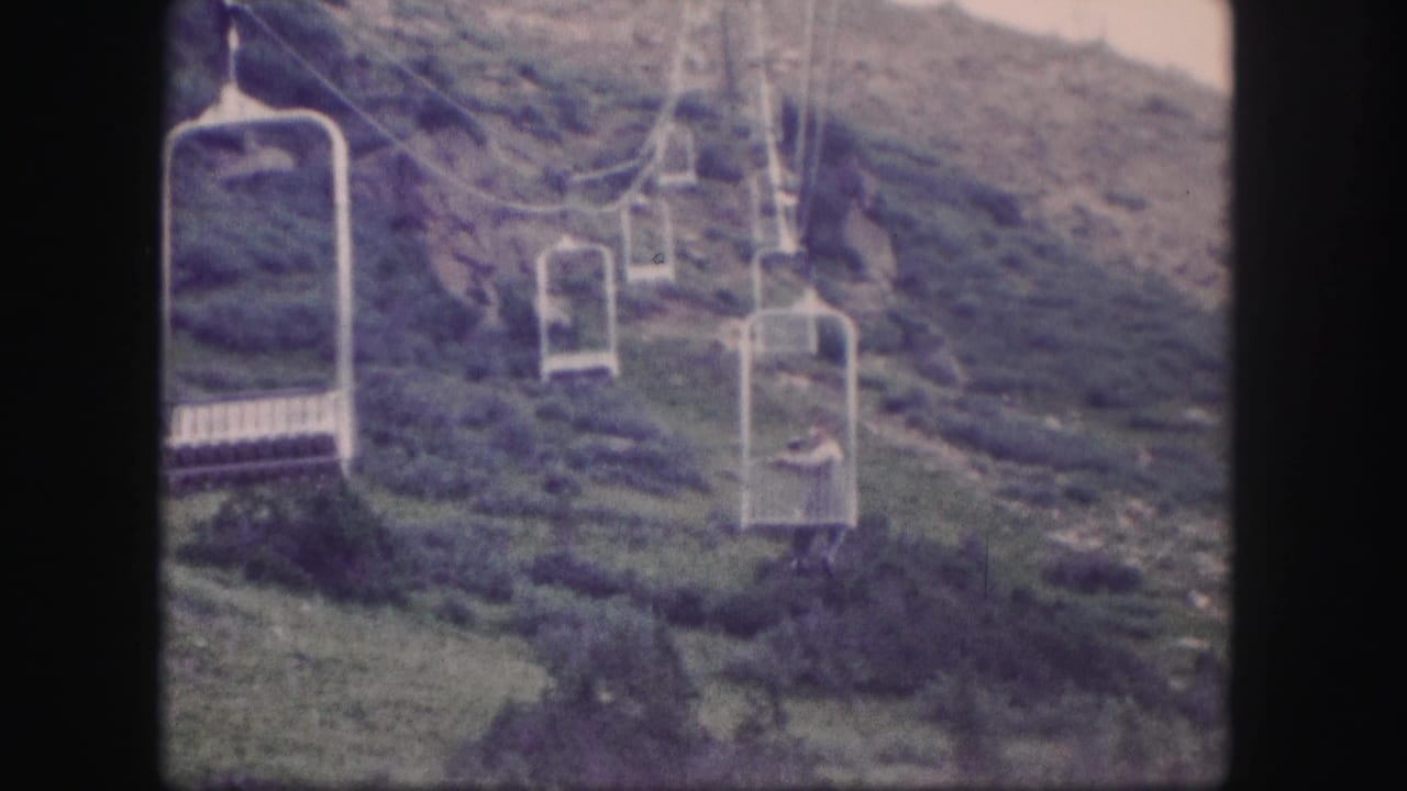 Chairlift seats and cables pass over a grassy hillside with rocky patches.